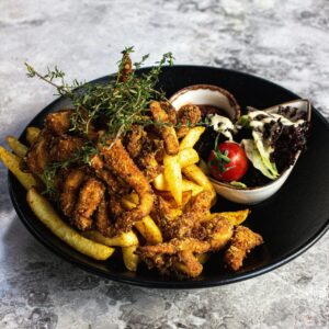 A savory platter of fried chicken with fries and salad on a black plate, perfect for food lovers.