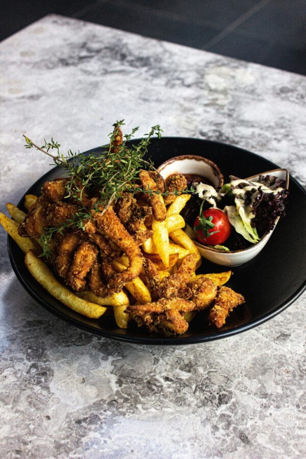 A savory platter of fried chicken with fries and salad on a black plate, perfect for food lovers.