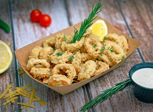 Delicious crispy fried calamari served with lemon and dipping sauce on wooden table.