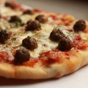 Close-up of a tasty meatball pizza slice with melted cheese and herbs.