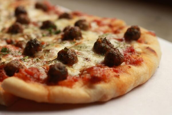 Close-up of a tasty meatball pizza slice with melted cheese and herbs.