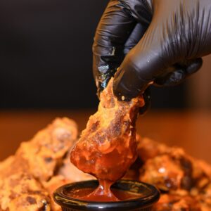 Close-up of crispy chicken wing dipped in hot sauce, perfect for food lovers.