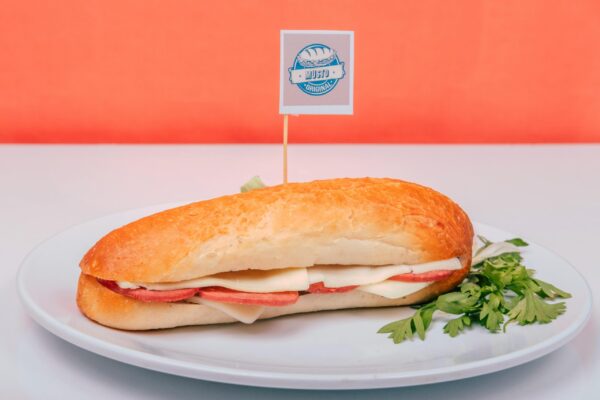 Close-up of a fresh Italian sub sandwich with cheese and salami on a white plate with parsley garnish.
