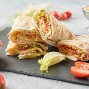 A tempting display of shawarma wraps with fresh lettuce, tomato, and sauce on a slate board.