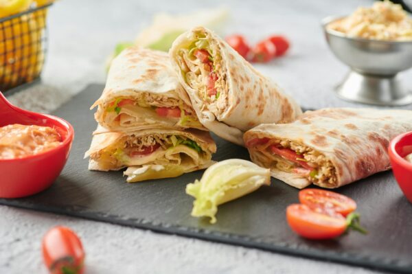 A tempting display of shawarma wraps with fresh lettuce, tomato, and sauce on a slate board.