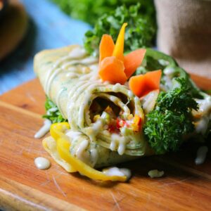 Close-up of a vibrant vegetable wrap garnished with fresh greens, served on a wooden board.