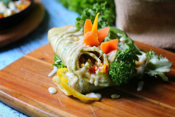 Close-up of a vibrant vegetable wrap garnished with fresh greens, served on a wooden board.
