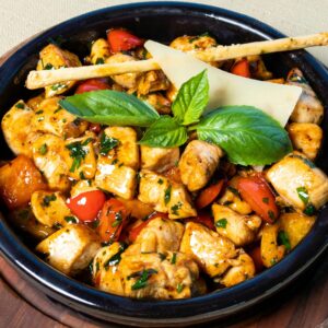 A vibrant grilled chicken salad garnished with fresh basil leaves and served in a rustic bowl.